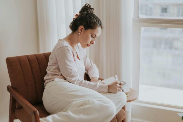 Woman writing in a notebook by a window.