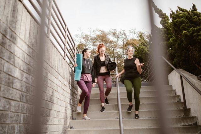 Three women walking down steps after a workout, carrying yoga mats